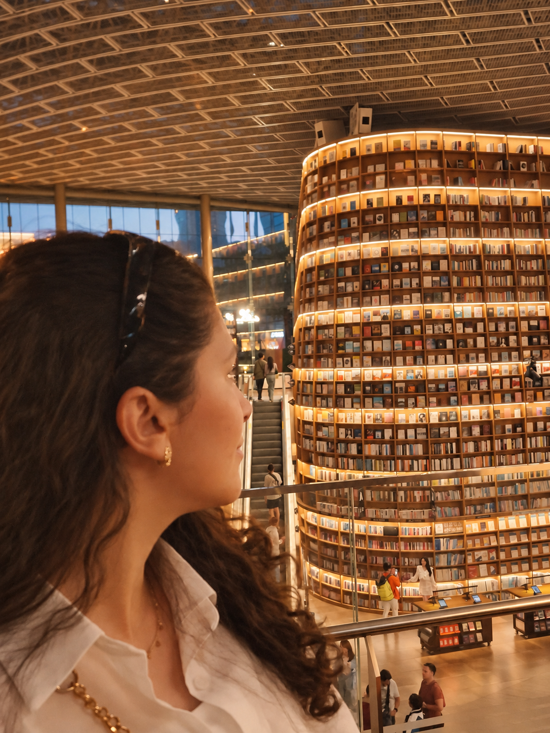 A reader looking toward a towering, warmly illuminated bookstore bookshelf